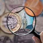 A magnifying glass held over a British one-pound coin and a ten-pound note featuring Big Ben, symbolizing a close analysis of the UK economy and the British Pound.
